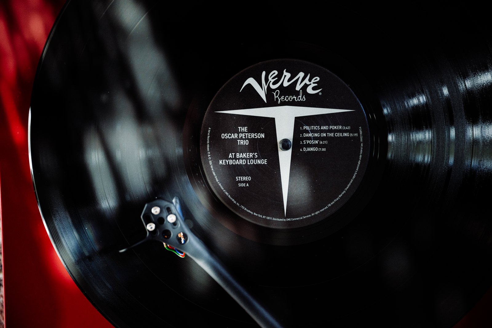 Macro close-up of the Verve Records label on the Oscar Peterson Trio At Baker's Keyboard Lounge LP, Side A, with the tonearm and stylus in playing position on the red Technics turntable at Kissa Kissa
