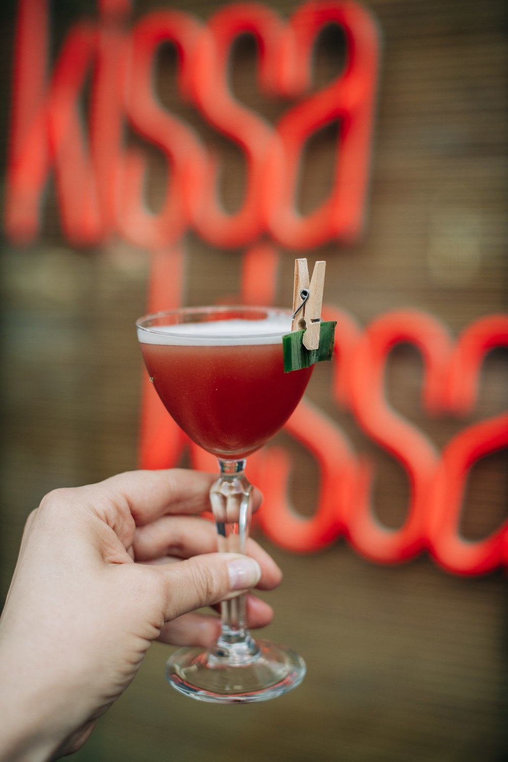 The So Nice pisco punch held in front of the Kissa Kissa neon sign, poured at Summer Samba, a bossa nova vinyl listening series in Crown Heights, Brooklyn