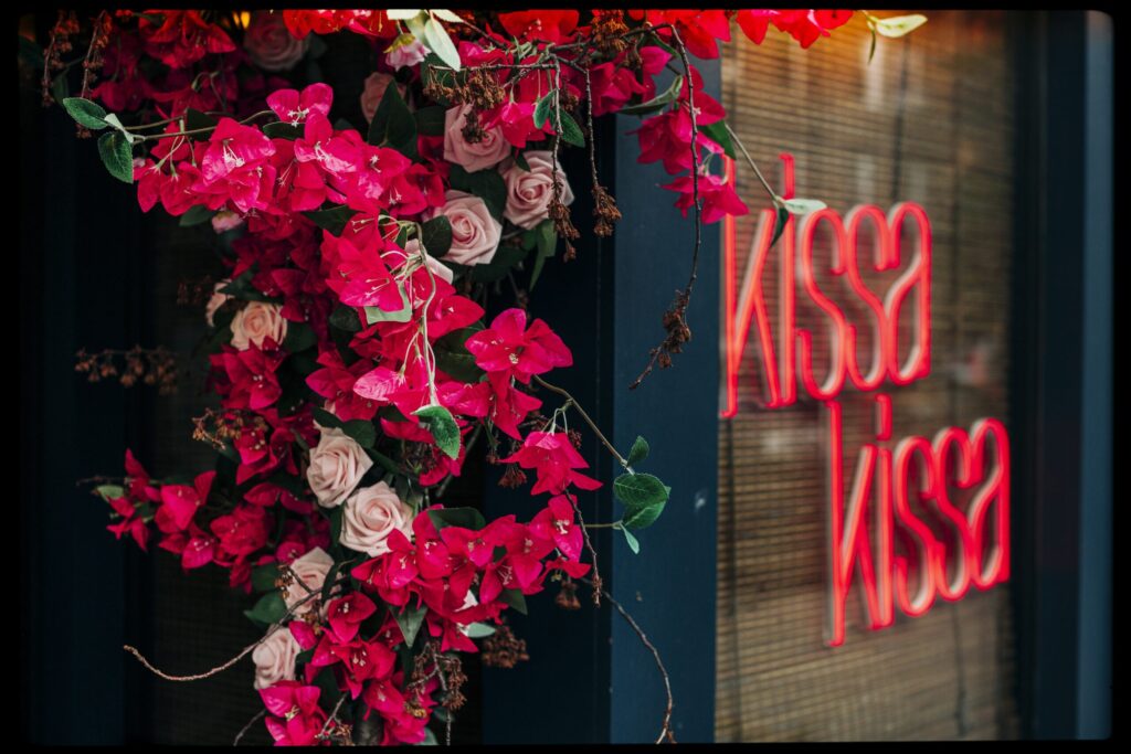 The Kissa Kissa neon sign framed by bougainvillea