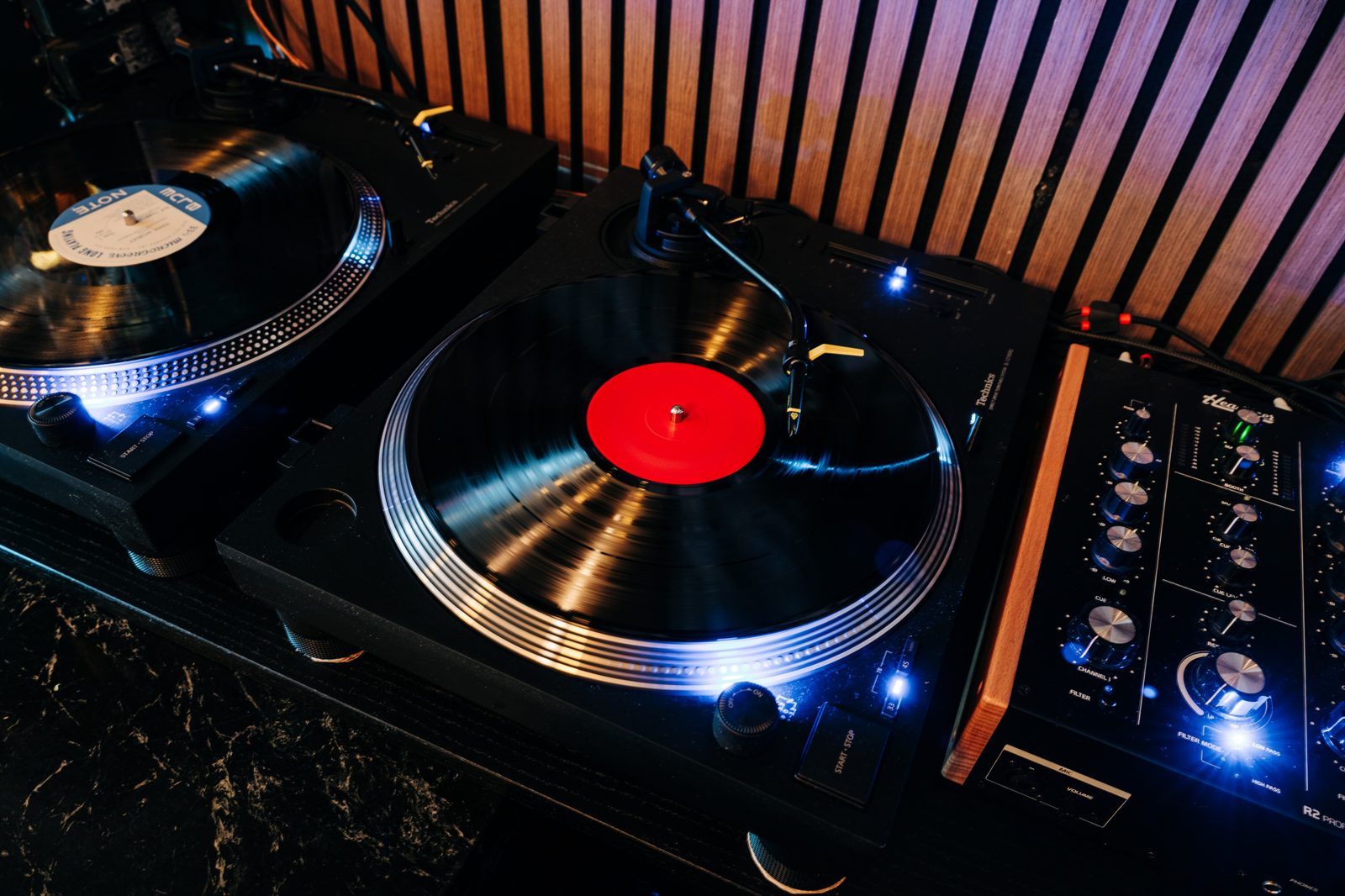 Two turntables behind the bar at Kissa Kissa, one playing a red-label LP with a yellow-lift Ortofon cartridge, beside the R2 rotary mixer